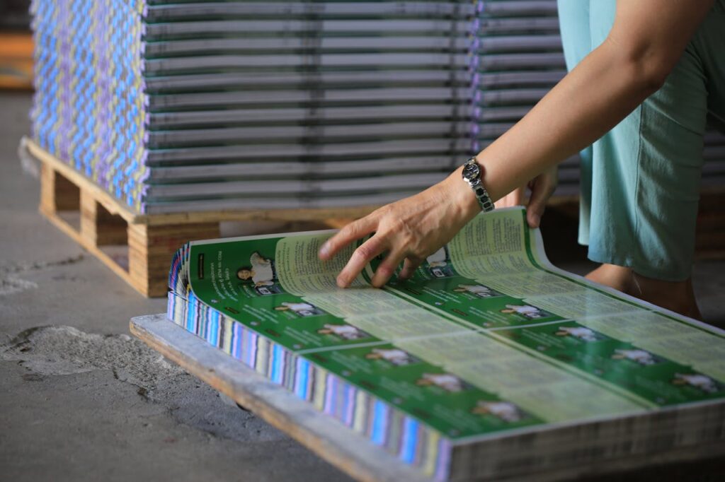 A person organizes stacks of printed publications in an industrial warehouse setting.